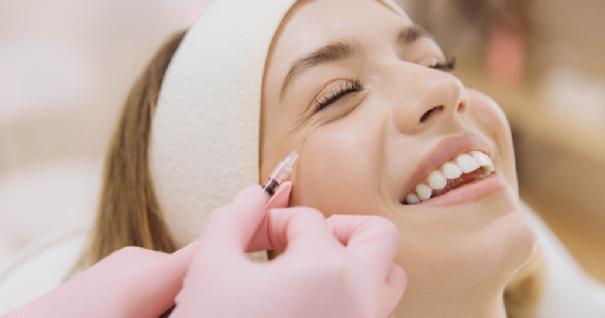 A smiling woman with a headband receives a Botox injection near her eye from a professional wearing pink gloves in St. Charles, IL